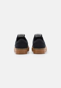 Schwarze Canvas-Sneaker mit flachem Schnitt und Gummisohlen, ausgestattet mit einer sandfarbenen Zwischensohle, weißem Branding an der Ferse und strukturiertem Stoff für besseren Halt.