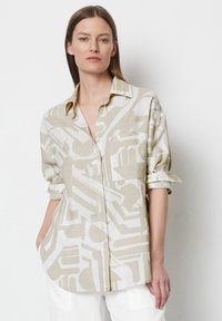 Linen button-up shirt in light beige with abstract white patterns. Features rolled sleeves and a relaxed fit. Straight cut hemline.