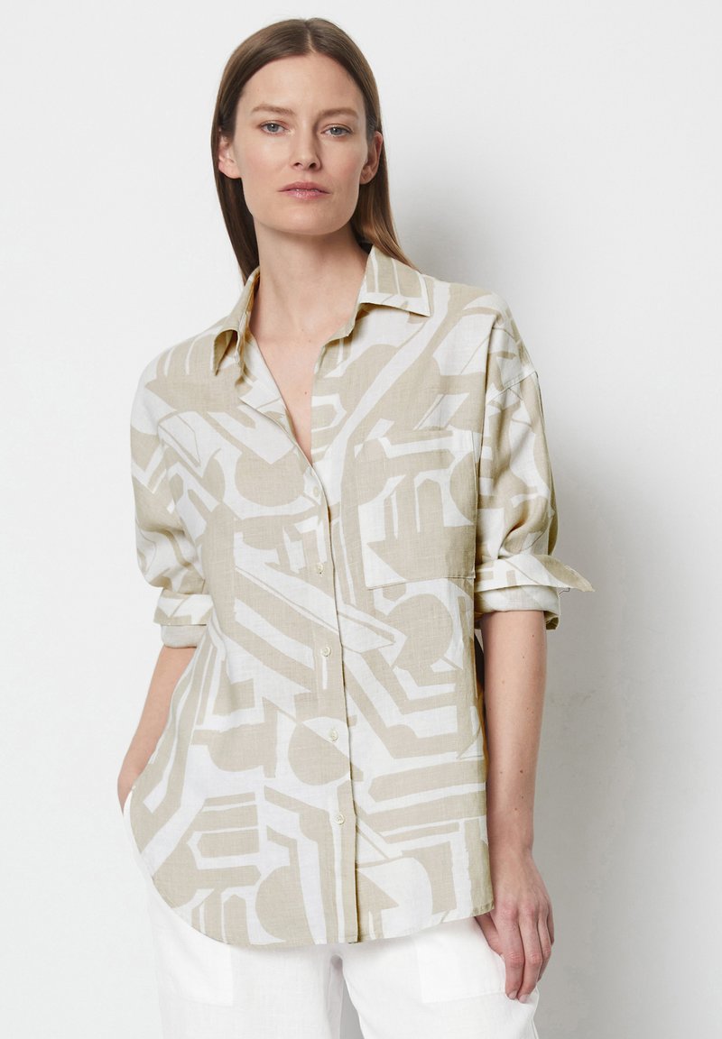 Linen button-up shirt in light beige with abstract white patterns. Features rolled sleeves and a relaxed fit. Straight cut hemline.