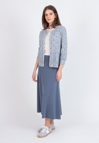 Cardigan azul claro con un patrón sobre una blusa blanca, combinado con una falda larga azul y zapatillas grises, presentando texturas suaves y un diseño sencillo.