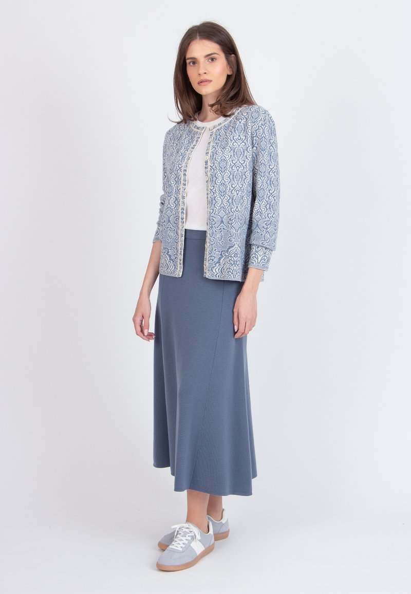 Vaaleansininen kuviollinen neuletakki valkoisen topin päällä, yhdistettynä pitkään siniseen hameeseen ja harmaisiin lenkkareihin, joissa on sileät pinnat ja yksinkertainen muotoilu.