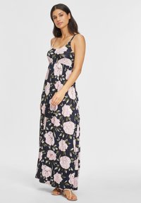 Floral Maxi-Kleid in Marineblau mit rosa Pfingstrosenmuster. Es verfügt über dünne Träger, eine lockere Passform und einen fließenden Saum. Getragen mit Riemchensandalen.