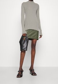 Lysegrå ribstrikket sweater med lange ærmer, olivengrøn læder mininederdel, sort vinkel taske og sorte åbne hæle.