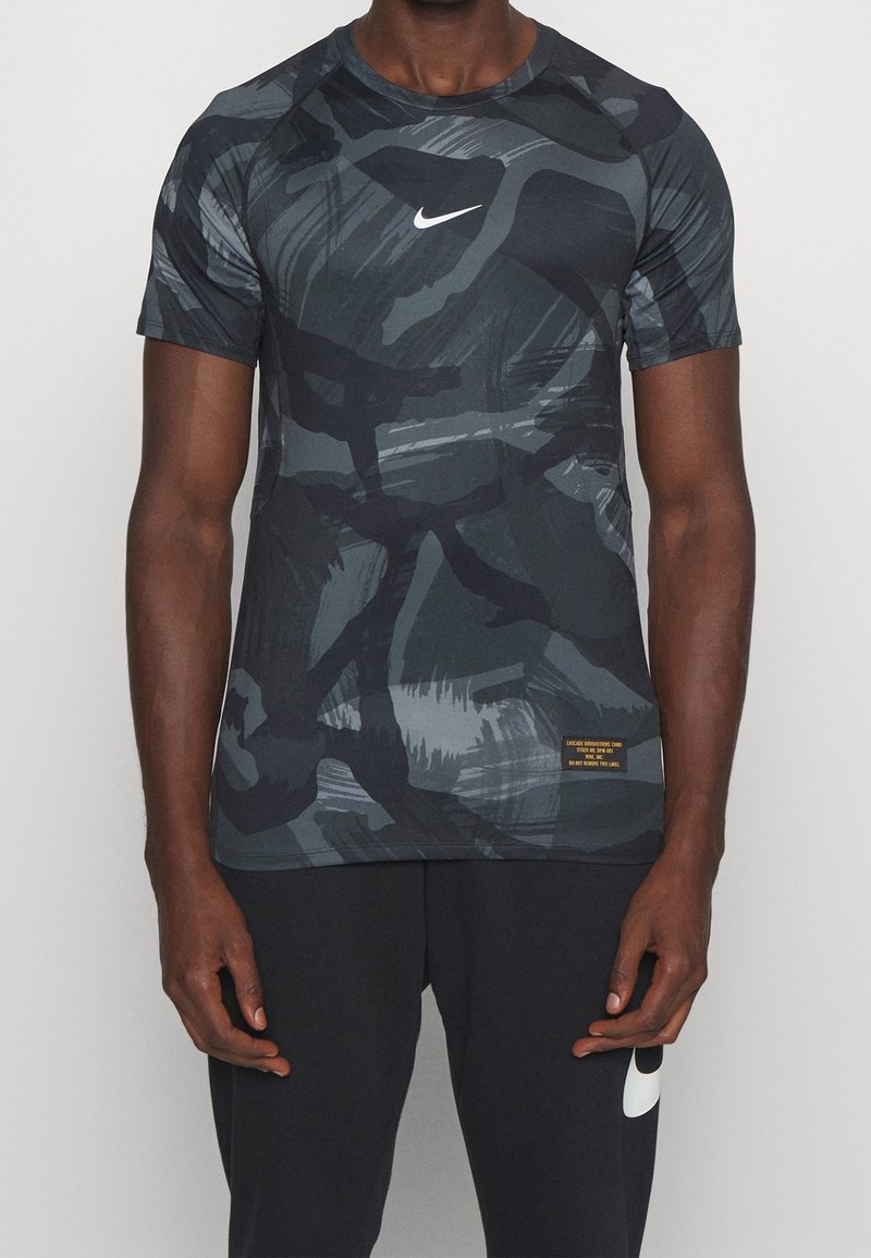 Camiseta deportiva de Nike de manga corta en gris oscuro con patrones de camuflaje abstractos. Tiene un cuello redondo y un pequeño logo blanco en el pecho.