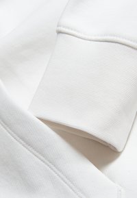 Tela blanca texturizada con primer plano de una prenda doblada, destacando las costuras y los finos detalles en el material y el diseño.