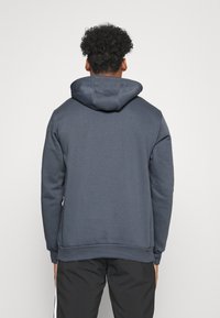 Hoodie gris foncé avec une grande capuche réglable. Fabriqué en tissu doux, il possède des poignets et un ourlet côtelés. Pas de motifs ou d'accent visible.