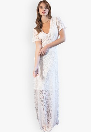 Lungo vestito bianco in pizzo con maniche corte, scollatura a V e silhouette fluida, caratterizzato da intricati motivi floreali e una parte inferiore trasparente.