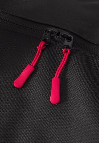 Primer plano de una cremallera negra sobre una tela negra con dos cuerdas rojas unidas a los deslizadores de la cremallera.