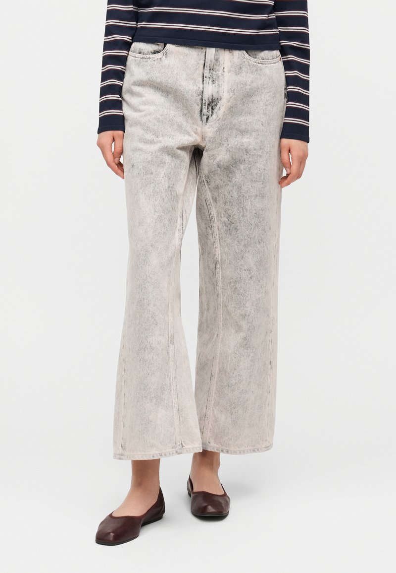 Ανοιχτό γκρι τζιν παντελόνι φαρδιάς γραμμής με ξ εθωριασμένο φινίρισμα, διαθέτει μπροστινές τσέπες και εμφανείς ραφές. Συνδυασμένο με σκούρα επίπεδα παπούτσια.