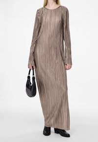 Robe longue à côtes de couleur taupe, fabriquée dans un tissu texturé. Associée à un petit sac à main noir et des bottes à talons noires.