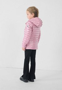 Giacca imbottita rosa con cappuccio, caratterizzata da un motivo a quadri diagonali e logo sulla manica, abbinata a pantaloni neri a zampa d'elefante e scarpe nere.