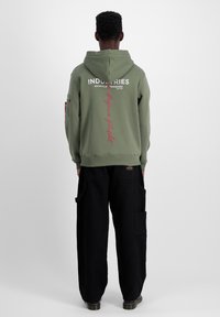 Tricou cu glugă de culoare verde măsliniu, cu text și accente albe și roșii; asortat cu pantaloni cargo negri, cu croi lejer și multiple buzunare.
