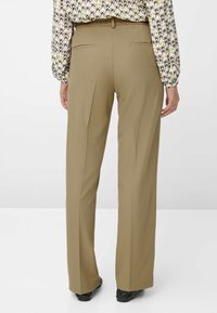 Pantaloni kaki a gamba larga con una texture liscia, dotati di doppie tasche posteriori e una vita a metà altezza. Abbinati a una blusa stampata.