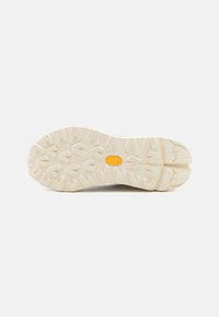 White outsole with textured surface, featuring a zigzag pattern and a yellow logo at the center. Multi-directional tread for traction.