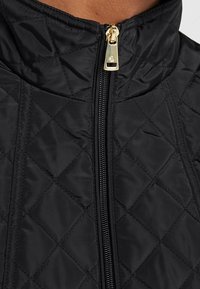 Närbild av svart vadderad jackkrage med guld blixtlås delvis draget i mitten.