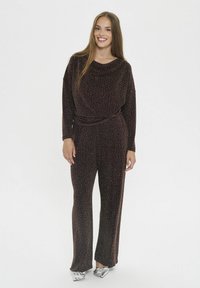 Jumpsuit lungo e morbido in velluto marrone scuro con accenti metalizzati a pois. Presenta un collo cowl e una cintura testurizzata coordinata.