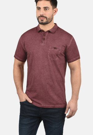 Bordo polo majica s opuštenim krojem, trobojnim patentnim zatvaračem, detaljem džepa i kratkim rukavima. Izrađena od mekog, teksturiranog materijala.