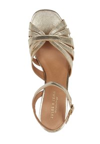 Gold metallic high-heeled sandals featuring crisscrossed straps, a square toe design, and a tan insole with the brand name embossed.