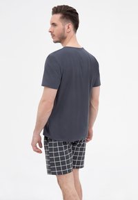 Szara koszulka z krótkim rękawem o okrągłym dekolcie, zestawiona z czarno-białymi krótkimi spodniami w kratę. Gładka tekstura, luźny krój.