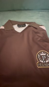 Rjavo polo majica s kontrastnim bež ovratnikom. Ima krožno vezeno logo z dvema in 'P' na levem prsnem delu.