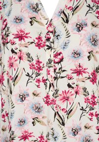 Tkanina s květinovým vzorem, která obsahuje růžové, modré a zelené květy na smetanovém pozadí, s výstřihem do V a dekorativními knoflíky.