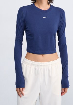 Person wearing a navy blue long-sleeve cropped Nike shirt paired with high-waisted white elastic waistband pants, torso visible.