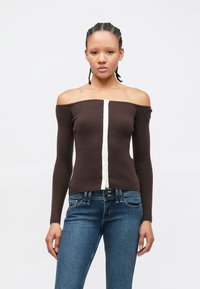 Haut marron côtelé à épaules dénudées avec une patte de boutonnage centrale crème. Associé à un jean en denim bleu, mettant en valeur un style décontracté.