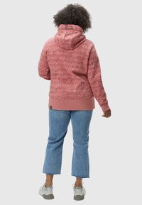 Felpa rosa con motivo a fantasia, dotata di cappuccio con coulisse, polsini e orlo a coste; abbinata a jeans cropped blu chiaro e sneakers grigie.