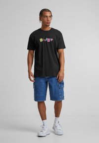Crna pamučna majica s višebojnim natpisom "homeboy", uparen s plavim traper kratkim hlačama i bijelim tenisicama. Opušteni outfit.