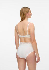 Λευκό σουτιέν και εσώρουχο με ψηλή μέση. Το σουτιέν έχει λεπτές τιράντες και κούμπωμα με άγκιστρα· το εσώρουχο διαθέτει ζώνη από δαντέλα και στερεό ύφασμα.