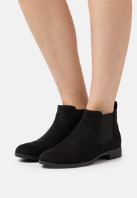 Black suede ankle boots feature elastic side panels and a low heel. The smooth texture contrasts with the matte finish of the sole.