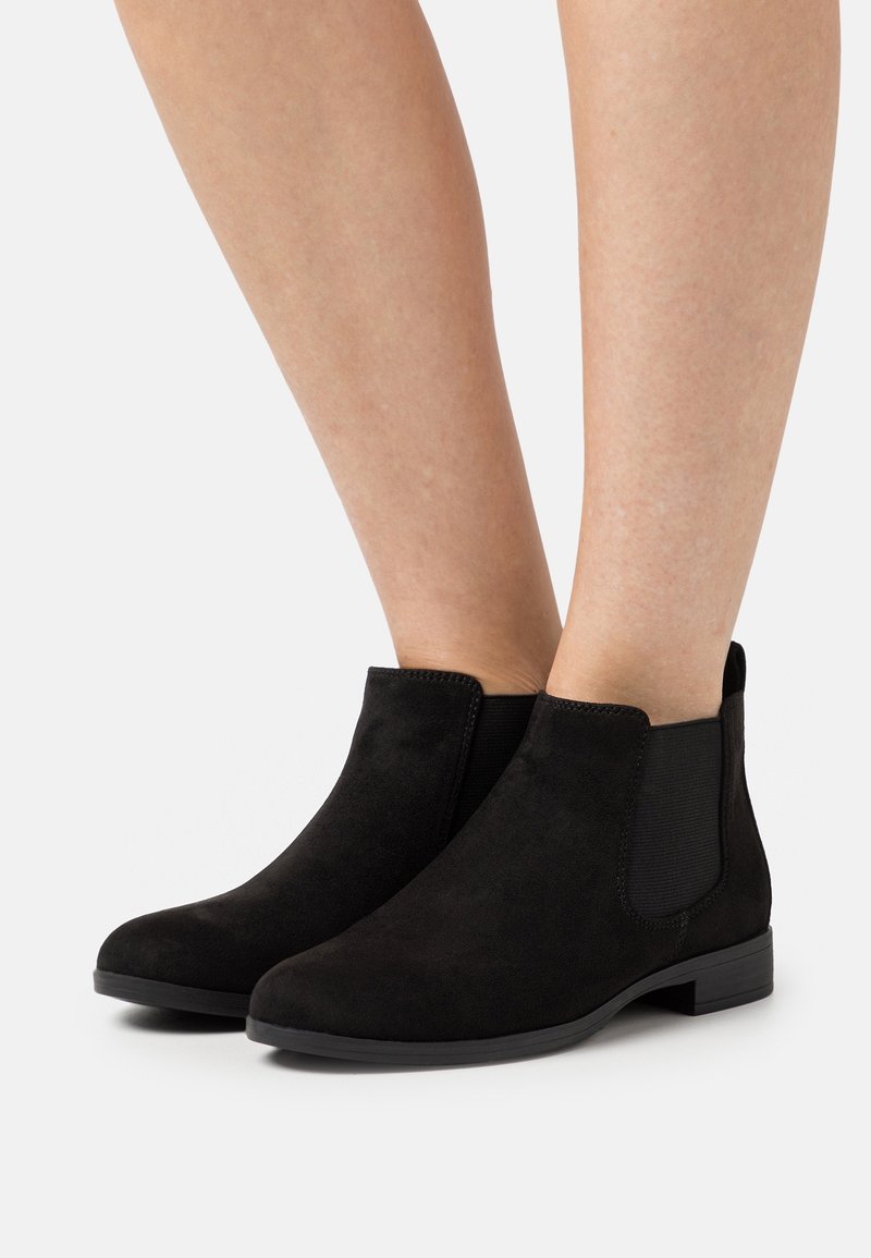 Black suede ankle boots feature elastic side panels and a low heel. The smooth texture contrasts with the matte finish of the sole.