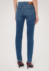 Modré džíny v úzkém střihu, s pěti kapsami a koženou nášivkou v barvě tan na pase. Dokončeno s vínovými botami na vysokém podpatku.