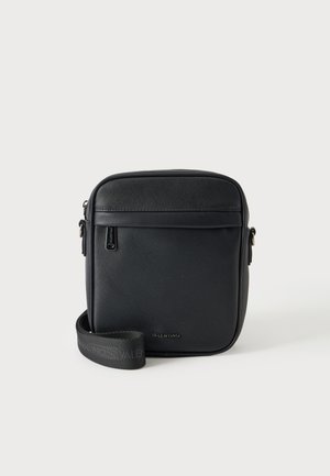 Petit sac bandoulière Valentino noir compact avec surface texturée, poche zippée frontale et bandoulière réglable avec logo sur fond uni.