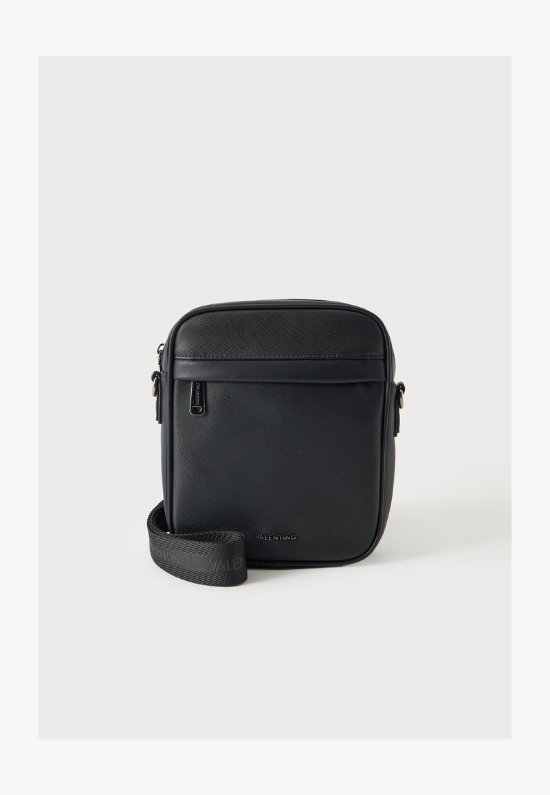 Κομψή μαύρη τσάντα Valentino crossbody με υφή επιφάνειας, μπροστινή τσέπη με φερμουάρ και ρυθμιζόμενο λουρί ώμου με λογότυπο, σε μονόχρωμο φόντο.