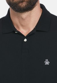 Black polo shirt made of textured cotton, featuring a classic collar, two-button placket, and a small penguin logo on the left chest.