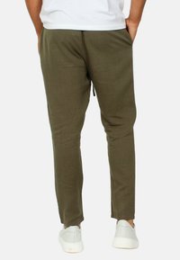 Pantaloni in tessuto leggero verde oliva con vita regolabile, gambe affusolate, tasche laterali e vestibilità casual, abbinati a scarpe bianche.