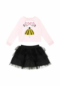 Roza dukserica s grafiko mačke, ki nosi očala v obliki srca, v kombinaciji s črno večplastno til krilom. Obleka vključuje živahne barve in teksture.