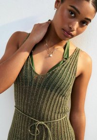 Abito lavorato a maglia verde oliva con righe verticali, scollatura a v e vita con fiocco. Presenta un top verde a strati sotto. Tessuto testurizzato.