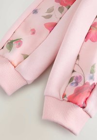 Sweatshirt rose avec des manches en satin à motifs floraux, des poignets côtelés et un corps en coton doux. Présente des roses bien visibles et de petites accents floraux.
