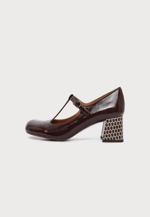 Chaussure Mary Jane en cuir verni marron foncé avec bride en T et talon bloc à motif sur fond uni.