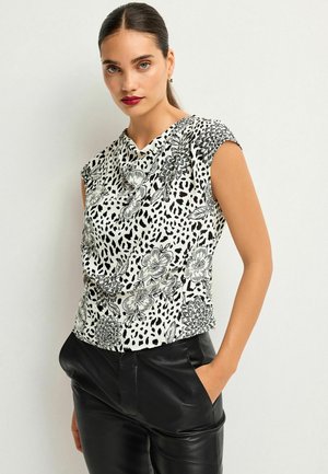 Top a maniche corte bianco con motivi floreali e maculati neri. Tessuto morbido con scollatura drappeggiata, abbinato a pantaloni in pelle nera.