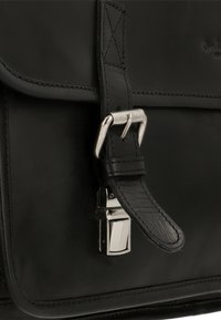 Black leather bag featuring a smooth texture, rectangular shape, a metal buckle closure, and contrasting stitching along the edges.