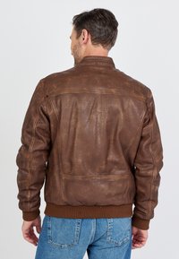 Bruine leren bomberjack met ribbelboorden en -zoom, met een gladde textuur en zichtbare naden op de achterkant.