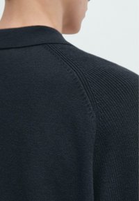 Maglione a maglia blu navy con collo, cuciture testurizzate sulle spalle e finitura liscia. La vista posteriore mette in evidenza la maestria artigianale.