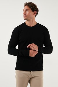 Maglietta nera a maniche lunghe, in maglia a coste, con scollatura rotonda, design aderente e tessuto testurizzato, indossata con pantaloni chiari.