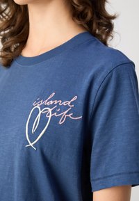 Navy blue cotton t-shirt with a crew neckline and short sleeves. Features embroidered text "island life" in pink and white with a heart design.