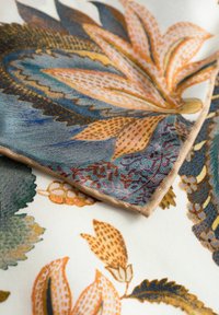Tissu à motif floral présentant des couleurs vives comme l'or, le vert et le bleu, avec une texture lisse et des bords beiges.