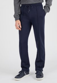 Pantalones de chándal azul marino de tejido suave con cintura ajustable, bolsillos laterales y un detalle de ribete sutil. Combinados con zapatillas azul marino.