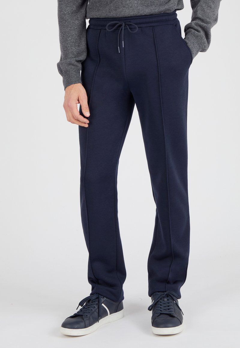 Pantalones de chándal azul marino de tejido suave con cintura ajustable, bolsillos laterales y un detalle de ribete sutil. Combinados con zapatillas azul marino.